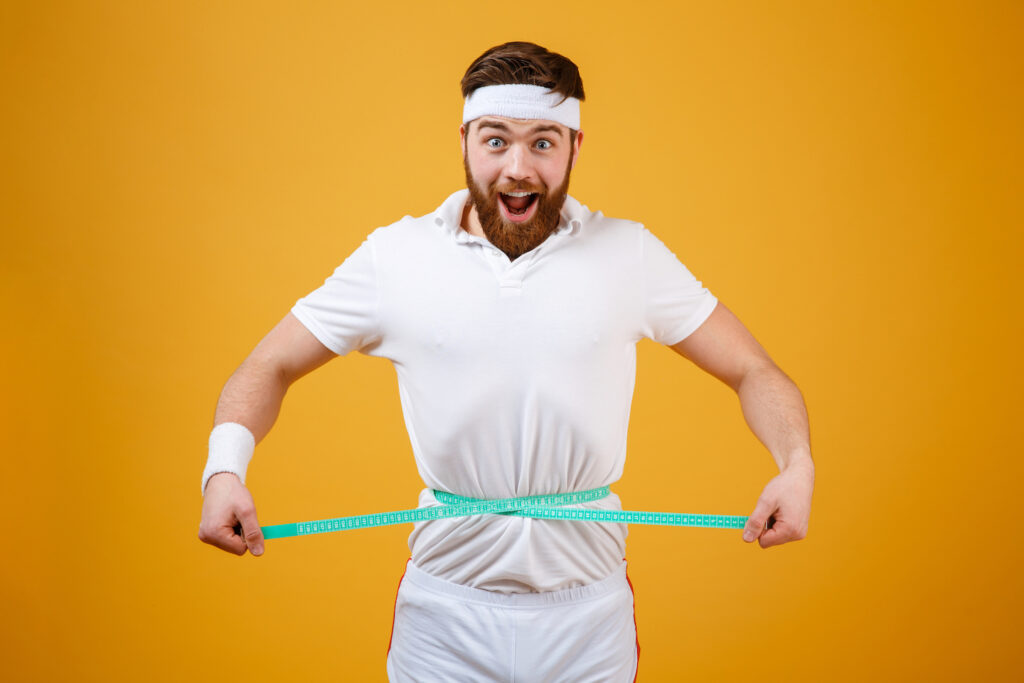 A person in a white shirt adjusts a turquoise measuring tape around their waist against a vibrant yellow background.