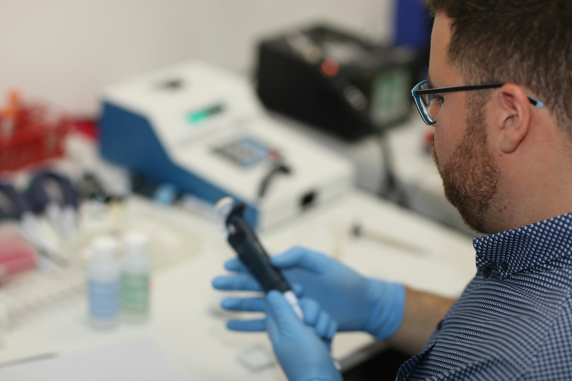 A lab technician in blue gloves holds a pipette, focused on their work at a clean workstation with scientific equipment.