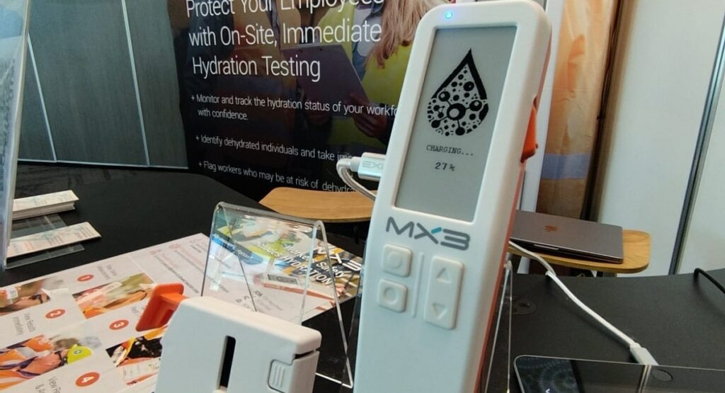 An MXC8 display device sits on a table, showcasing its sleek design and interface, with promotional materials in the background.