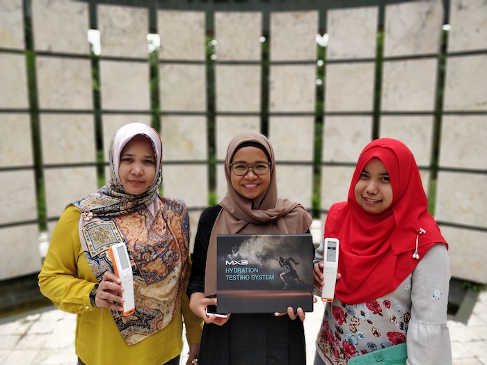Three women in hijabs proudly hold awards in front of a decorative wall, smiling and celebrating their achievements.