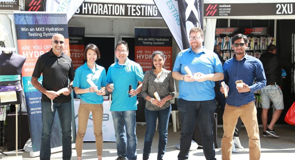 A group of six people smiling in front of an MX3 hydration testing display at the 2018 Melbourne Marathon.