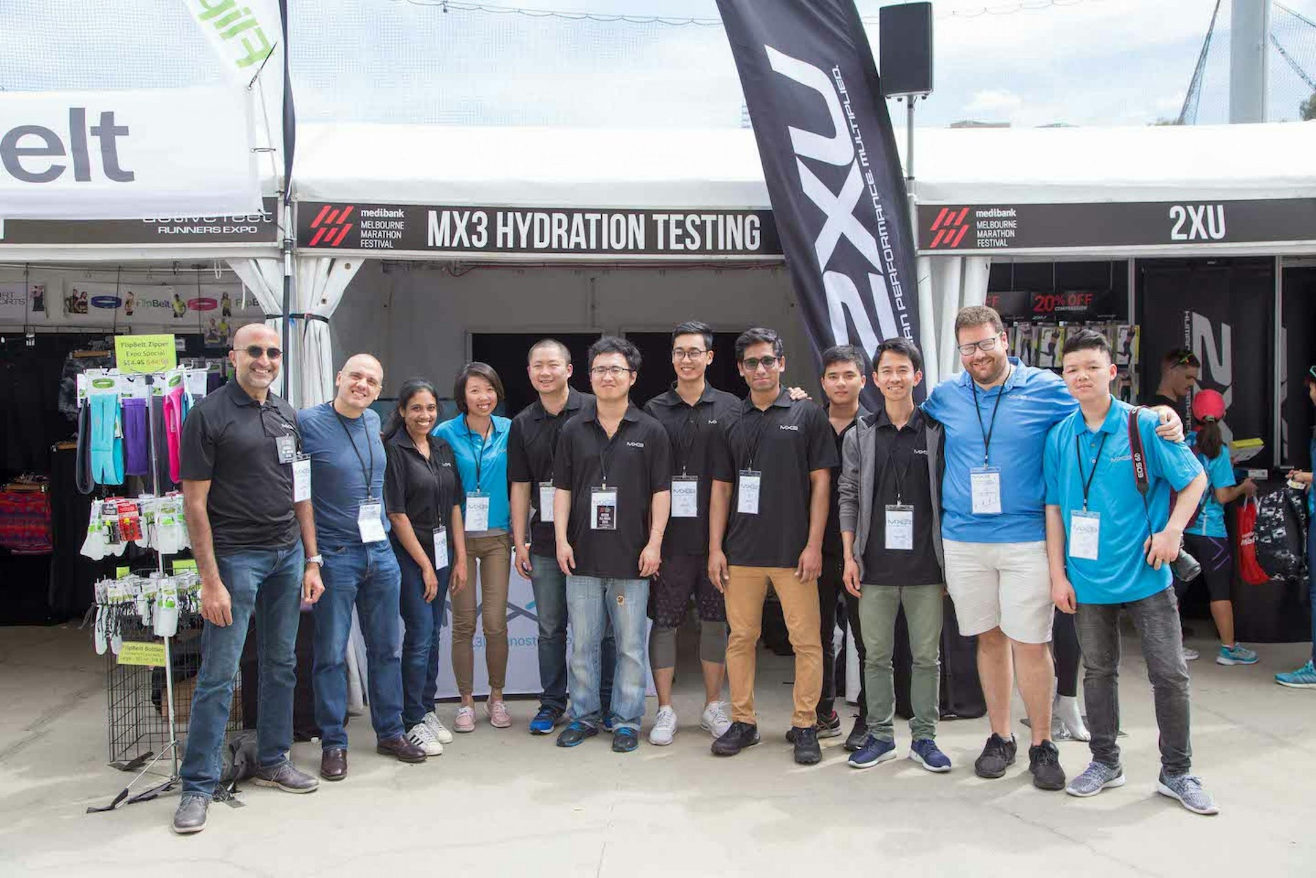 A diverse group of professionals in black and blue shirts poses together in front of a tent, smiling at an outdoor event.