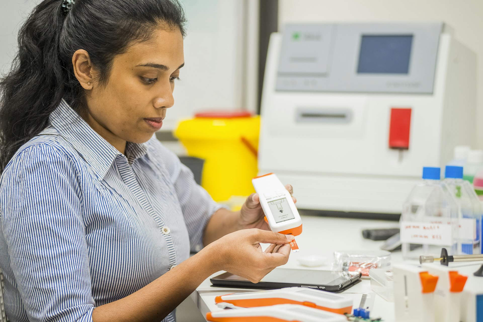 A person examines a small box while seated at a lab table, with scientific equipment and supplies in the background.