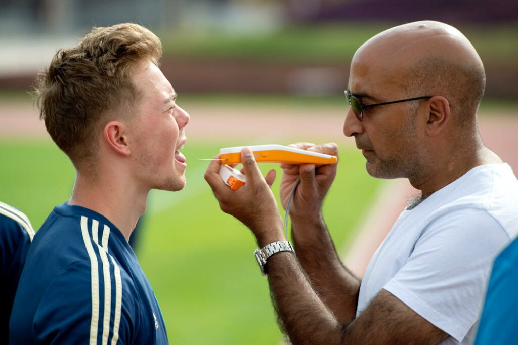 A person is feeding a slice of orange to another, both outdoors on a grassy field, showcasing a moment of bonding.