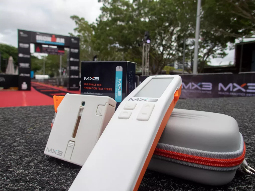 A close-up of various electronic devices and accessories on a table, with a blurred background of a sporting event setup.