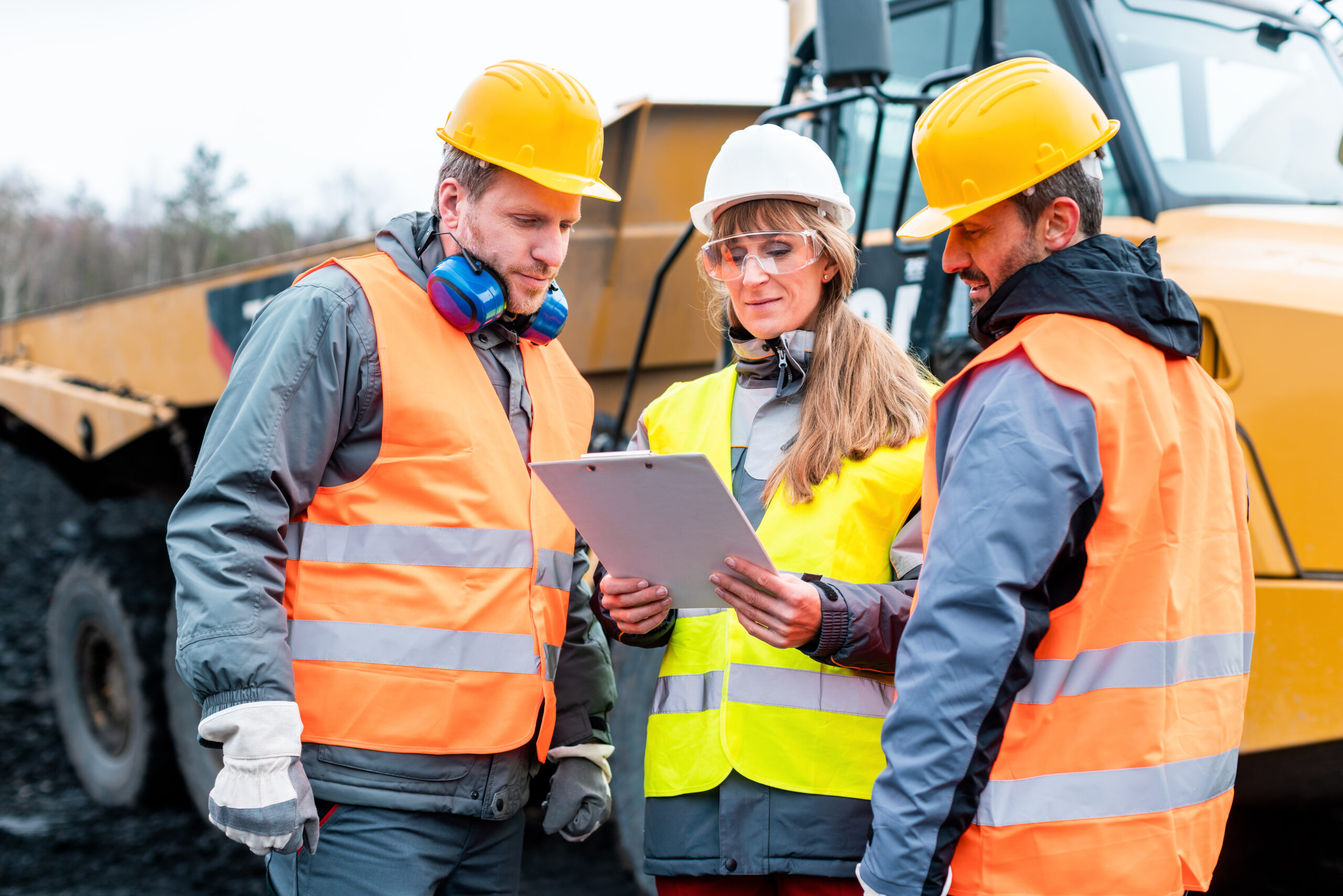 Three,Workers,In,A,Quarry,Discussing,In,Front,Of,Heavy